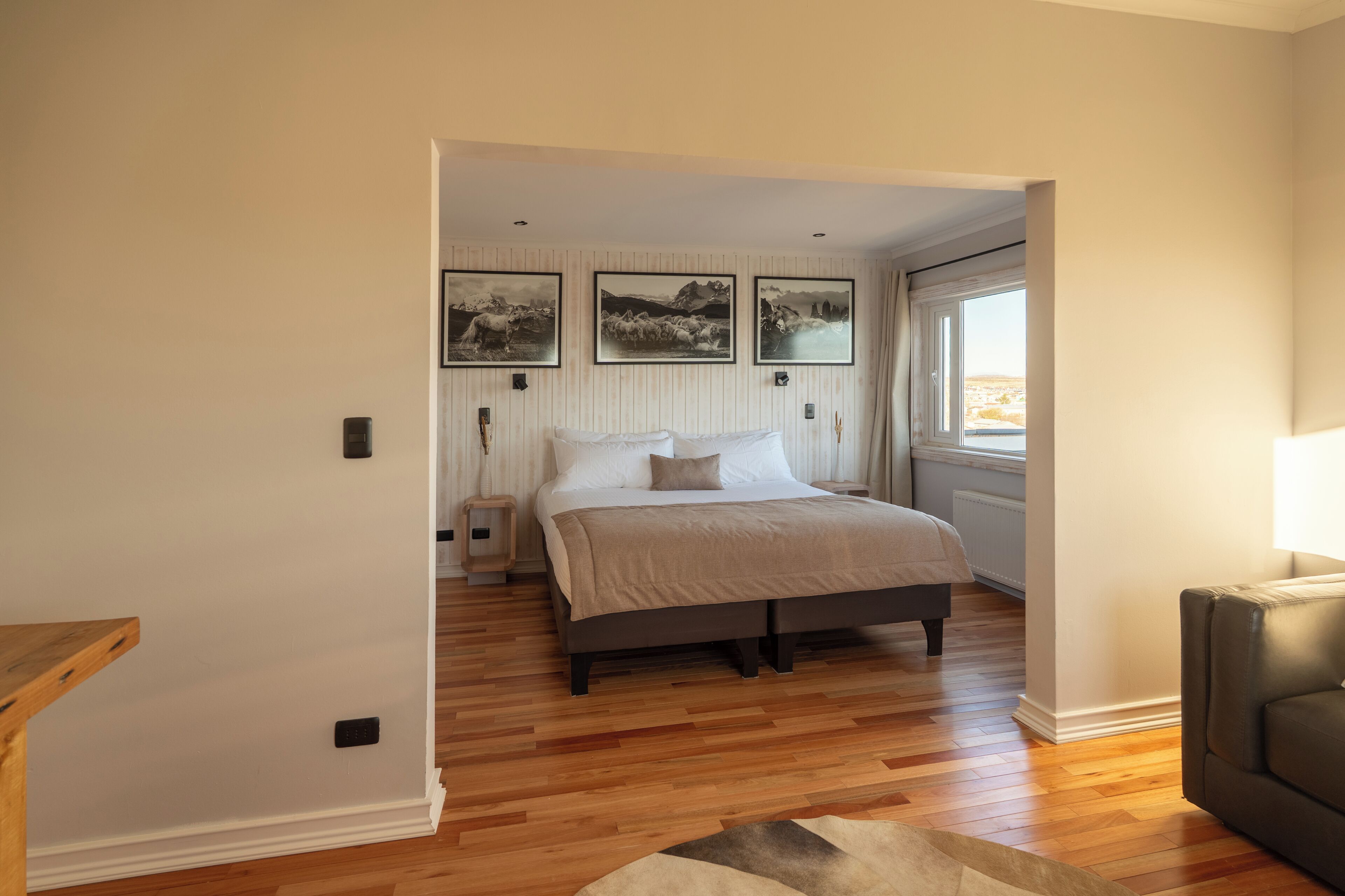 A bedroom with a bed, wooden flooring, a window, and wall-mounted artwork.