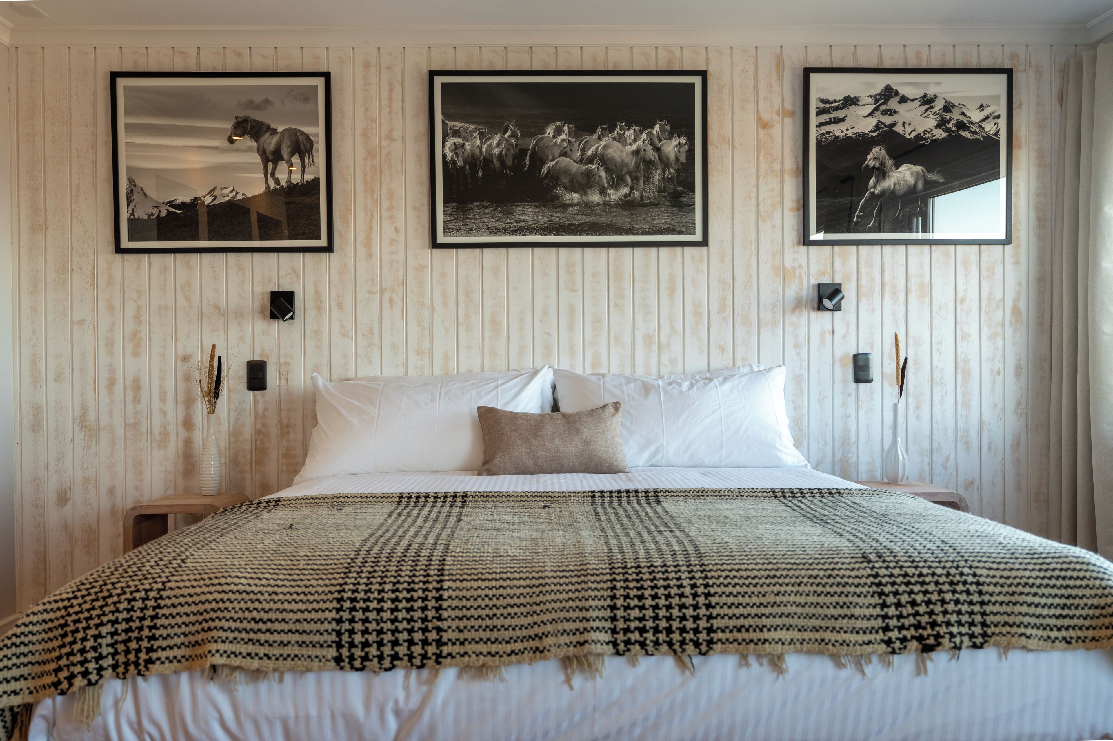 Habitación de hotel con una cama grande, tres fotografías enmarcadas en la pared y un diseño de panel de madera.
