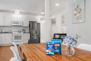 A modern kitchen with white cabinets and stainless steel appliances, a dining table with a vase of flowers, and a framed picture on the wall. - Comfy 3BR/2BA Lower Unit @Tukwila | Near Airport (Tukwila)