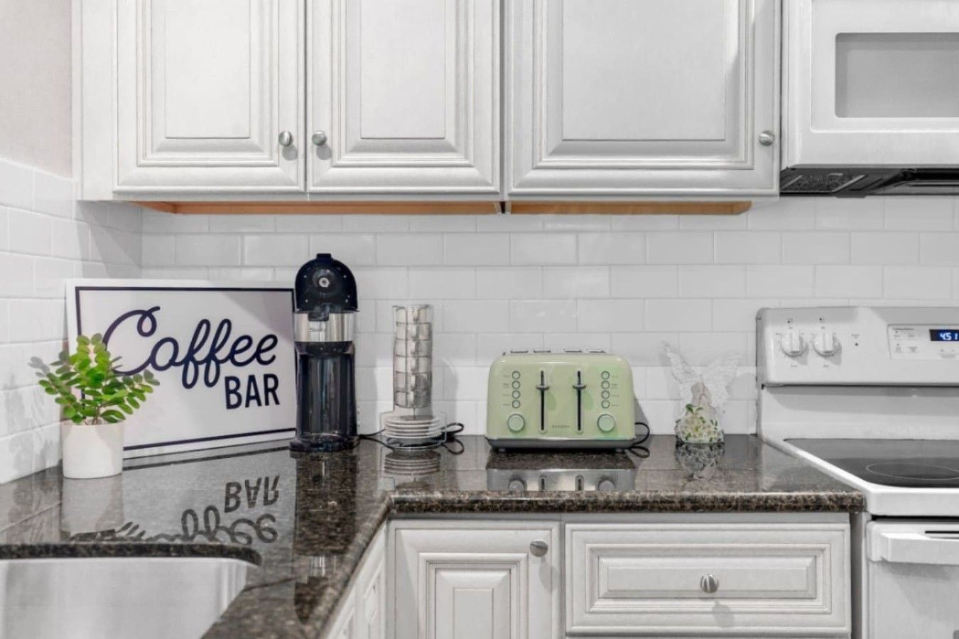 A kitchen with white cabinets, a coffee bar sign, a water dispenser, a toaster, and a stove.