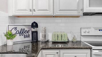 A kitchen with white cabinets, a coffee bar sign, a water dispenser, a toaster, and a stove.