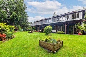 A two-story building with a balcony, surrounded by a well-maintained garden with a wooden planter and a hammock. - Comfy 3BR/2BA Lower Unit @Tukwila | Near Airport (Tukwila)