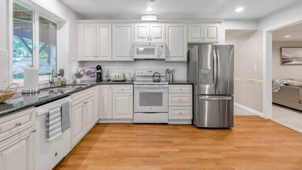 Una cocina moderna con armarios blancos, electrodomésticos de acero inoxidable y piso de madera.