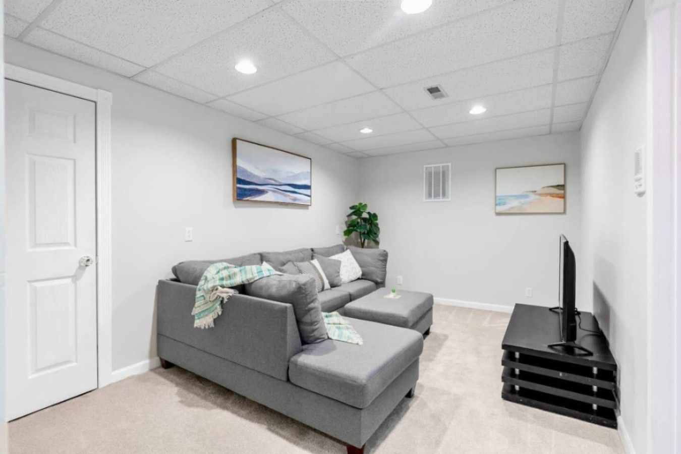 A living room with a grey sectional sofa, a flat-screen TV, and artwork on the walls.