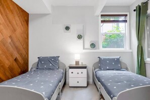 A bedroom with two beds, a nightstand, a window with curtains, and a wall-mounted plant. - Comfy 3BR/2BA Lower Unit @Tukwila | Near Airport (Tukwila)