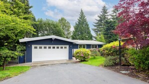 Edificio de una planta con garaje, rodeado de abundante vegetación y árboles.