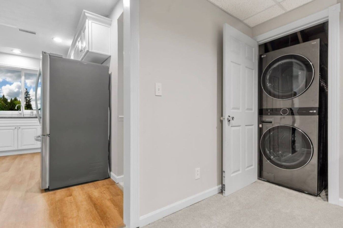 A laundry room with a front-loading washer and dryer, a gray refrigerator, and a white door.