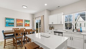 A modern kitchen with white cabinets, a central island, and a dining area with wooden chairs and a table. - New Build close to HPU, Furniture Mrkt & Downtown (High Point)