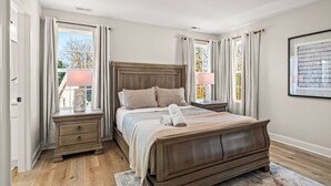 A bedroom with a wooden bed, two bedside tables, a nightstand, and a window with curtains. - New Build close to HPU, Furniture Mrkt & Downtown (High Point)