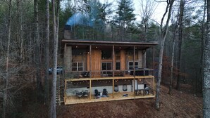 Eine zweistöckige Blockhütte mit Balkon und Außenbereich zum Sitzen, umgeben von einem Wald.