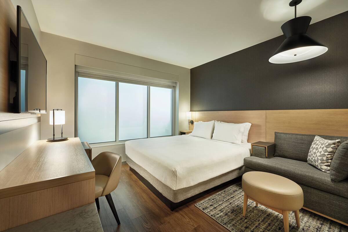 Een moderne hotelkamer met een groot bed, een bureau, een bank en een groot raam.