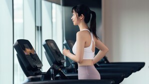 Een vrouw die op een loopband loopt in een sportschool met grote ramen en trainingsapparatuur.