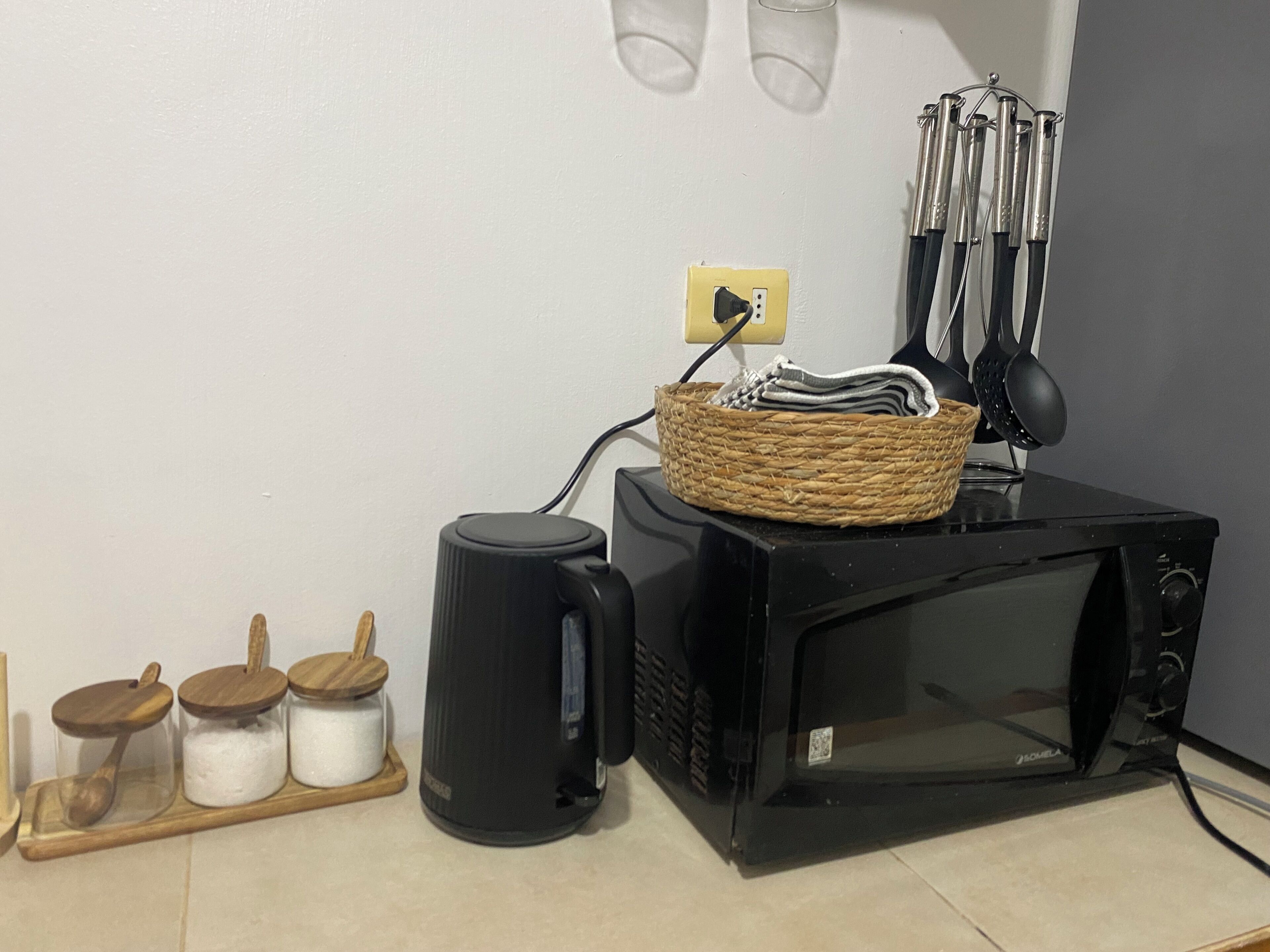 A kitchen with a microwave, a kettle, and a basket on the counter.