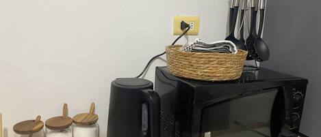 A kitchen with a microwave, a kettle, and a basket on the counter.