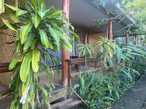 A covered outdoor area with wooden beams, a stone wall, and various green plants.