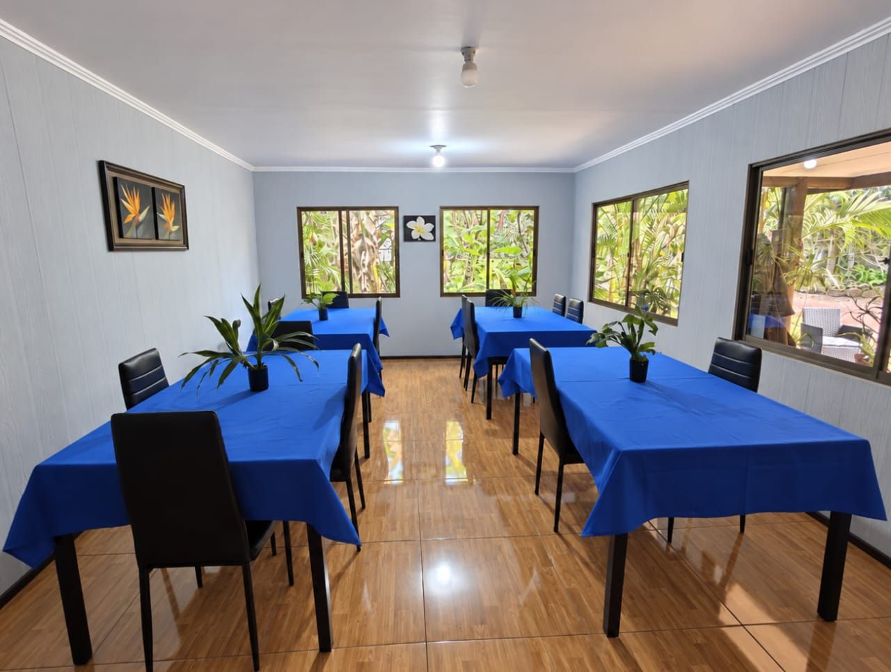 A conference room with multiple tables and chairs, large windows with a view of greenery, and a ceiling light fixture.