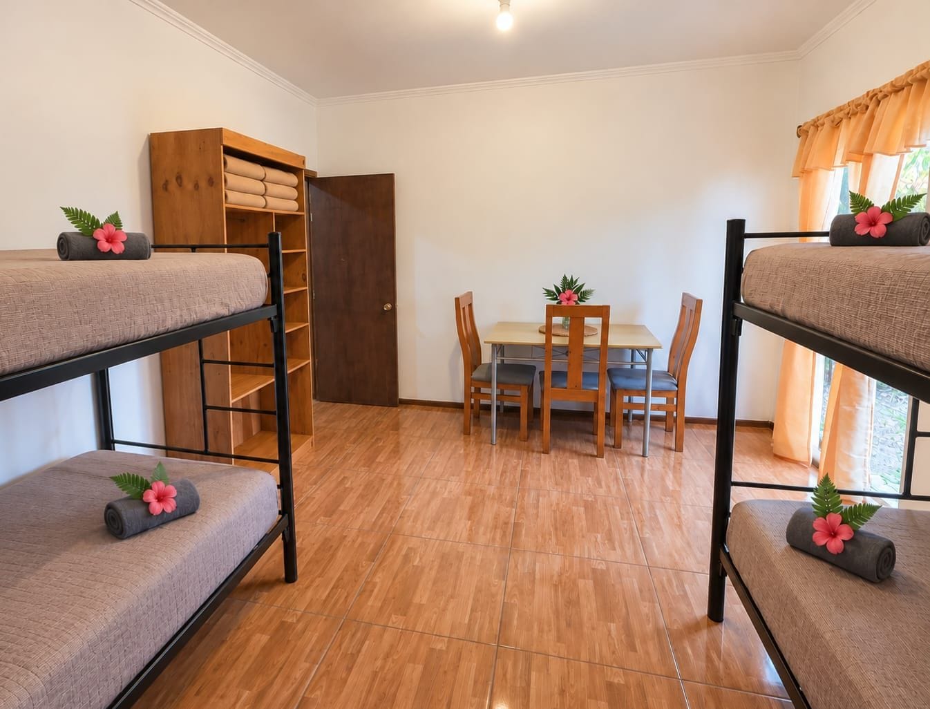 Ein Schlafsaalzimmer mit Etagenbetten, einem Holzschrank, einem Esstisch mit Stühlen und einer Tür.