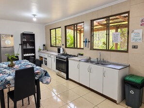 A kitchen with a dining table, chairs, a stove, a sink, and a trash bin.