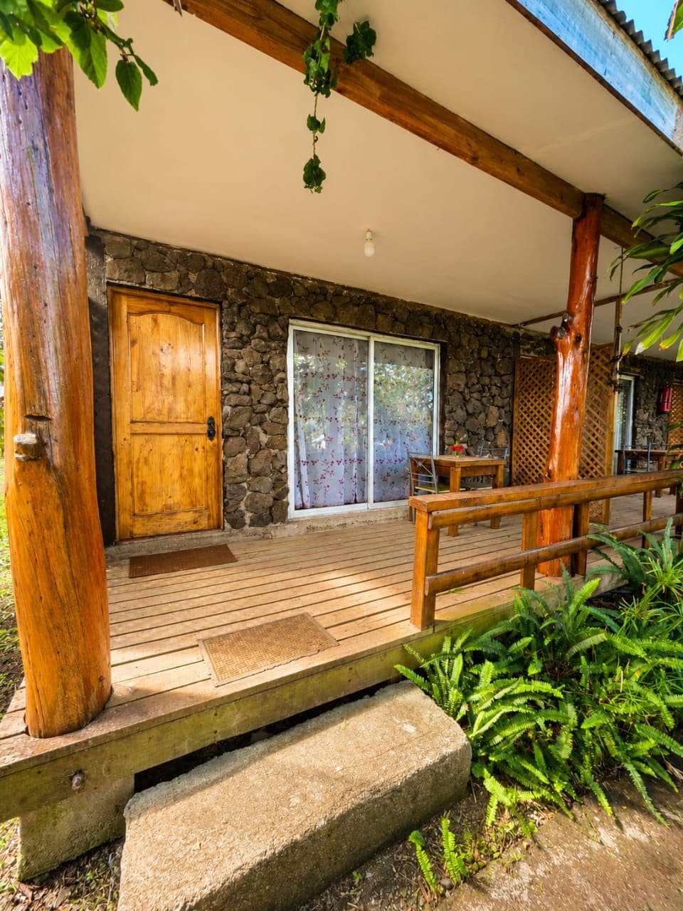 A wooden deck leading to a stone building with a wooden door and a sliding glass door.