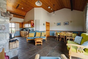 A spacious living area with a stone fireplace, wooden furniture, and a kitchen in the background.