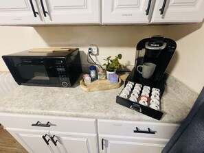 Una encimera de cocina con un microondas, una cafetera Keurig, una pequeña planta y una bandeja de cápsulas de café.