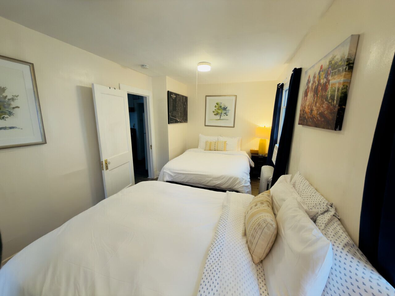 A hotel room with two beds, a nightstand, a lamp, and artwork on the walls.