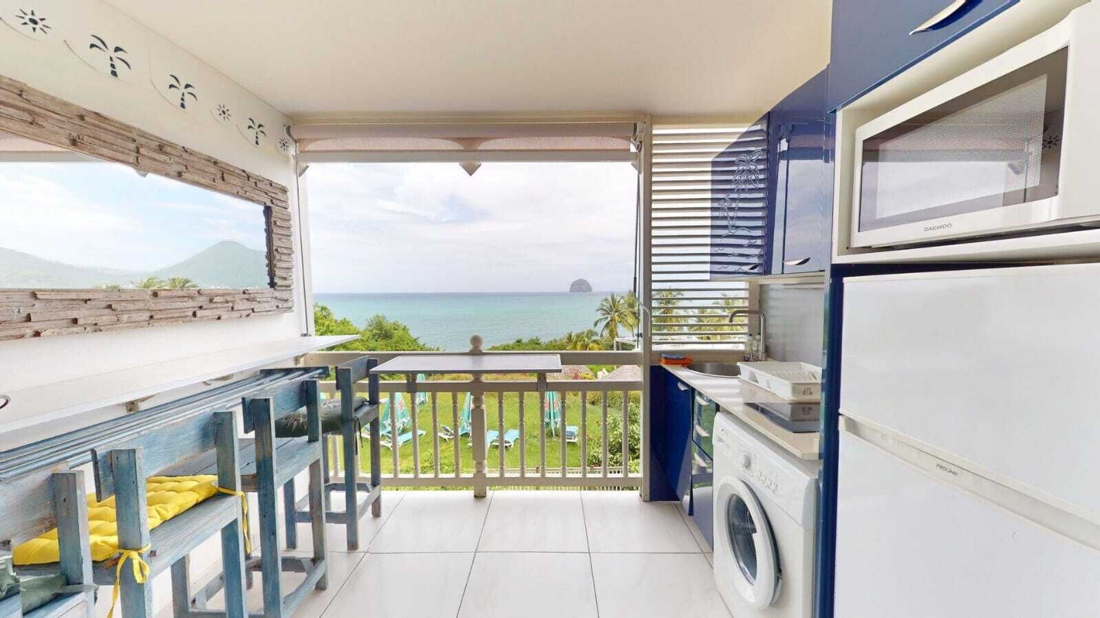 A balcony with a washing machine, a microwave, and a view of the ocean.