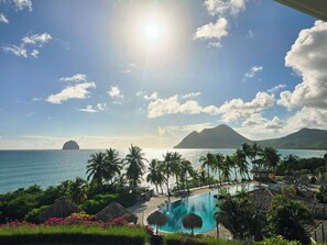 Un resort con piscina, palmeras y vistas al océano y a las montañas.