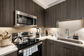 A modern kitchen with dark wood cabinets, stainless steel appliances, and a white countertop. - Velvet Lounge King Suite near Legacy West Pool (Plano)