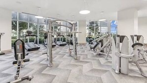 A gym with various exercise machines, large windows, and a chevron-patterned floor.