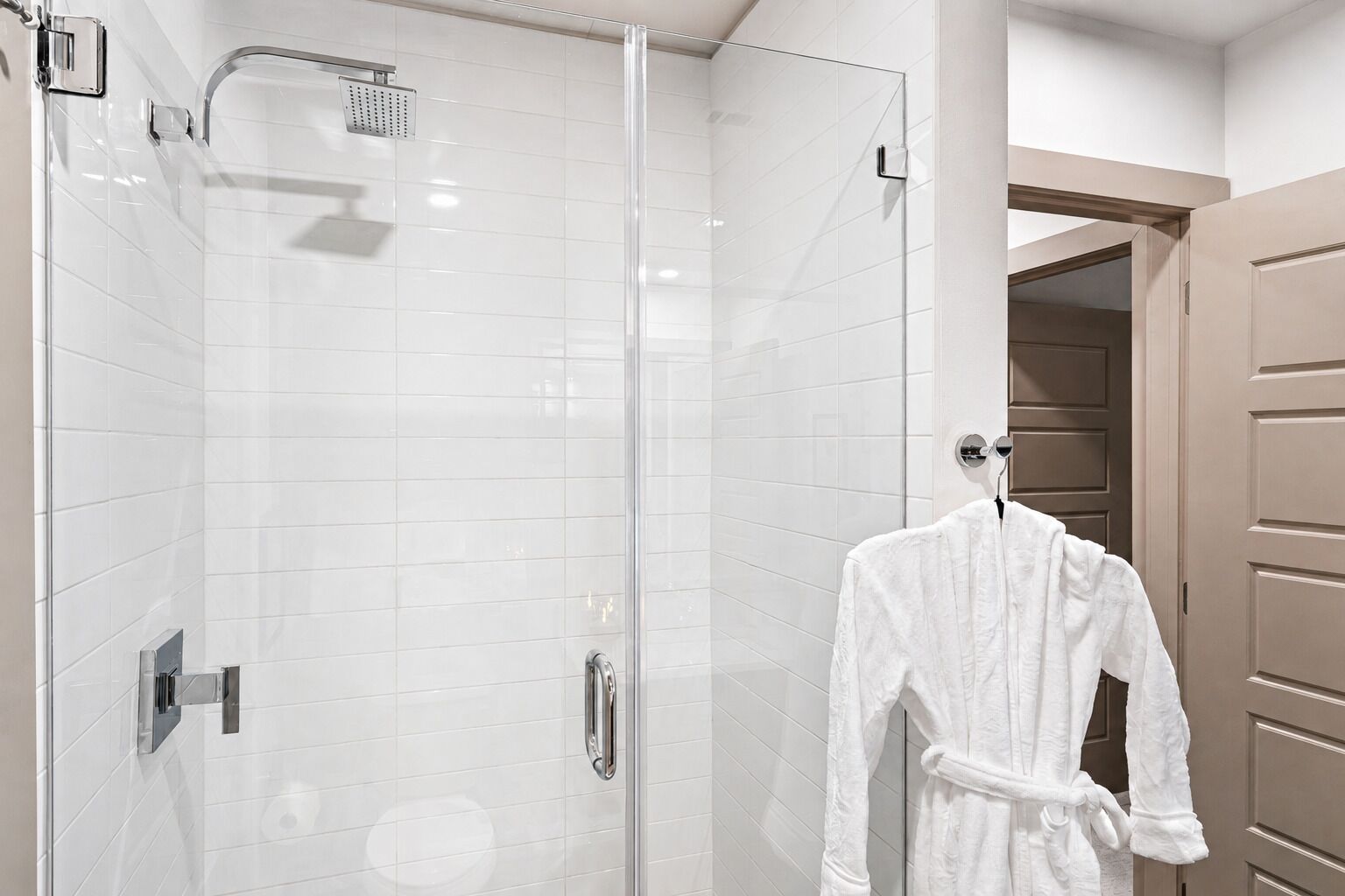 Ein modernes Badezimmer mit einer in Glas abgeschlossenen Dusche, einem Handtuchhalter und einer Holztür.