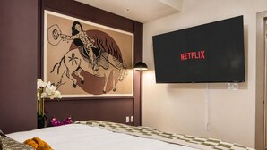 A hotel room with a bed, a wall-mounted TV displaying 'NETFLIX', and a large framed artwork above the bed.