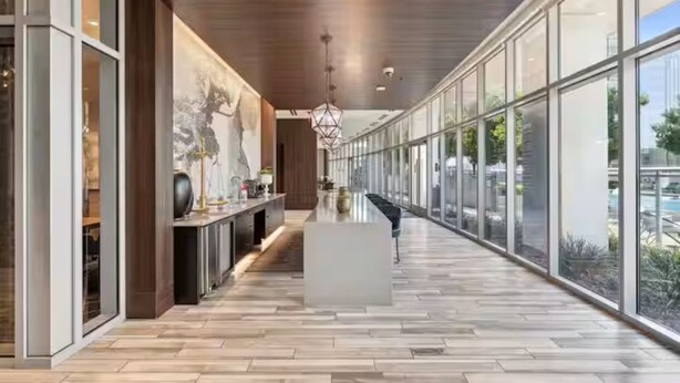 A modern hallway with a wooden floor, a central island, and large windows offering a view of the outdoors.