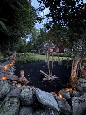 Un jardín con un sendero de piedra, una escultura de madera y una casa al fondo.