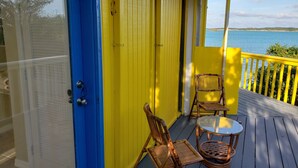 A bright yellow and blue exterior of a building with a wooden deck, two wicker chairs, and a glass table. - Bed and Beach - Newly Renovated Studio on the Beach near February Point Exuma (George Town)