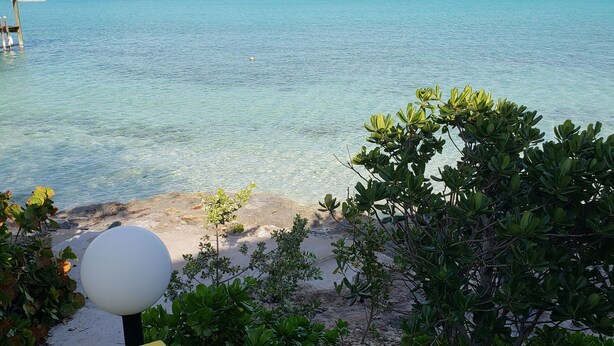A clear view of a beach with turquoise water, a wooden walkway, and a white lamp post. - Bed and Beach - Newly Renovated Studio on the Beach near February Point Exuma (George Town)