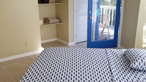 A bedroom with a bed, a ceiling fan, an air conditioning unit, a blue door, and a view of the outdoors. - Bed and Beach - Newly Renovated Studio on the Beach near February Point Exuma (George Town)