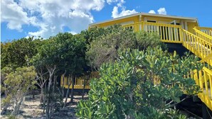 A yellow building with a staircase and a view of surrounding trees. - Bed and Beach - Newly Renovated Studio on the Beach near February Point Exuma (George Town)