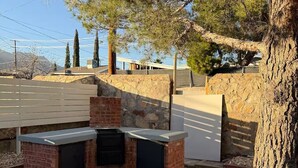 An outdoor barbecue area with a brick grill, surrounded by a stone wall and gravel. - Cozy Remodel 2 Story w/ King Bed / W/D / BBQ Patio (El Paso)