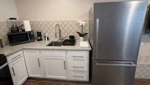 A kitchen with white cabinets, a stainless steel refrigerator, a microwave, a sink, and a small potted orchid. - Cozy Remodel 2 Story w/ King Bed / W/D / BBQ Patio (El Paso)