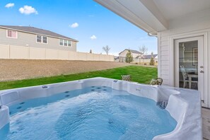 Un jacuzzi en un patio trasero con una casa y un césped al fondo.