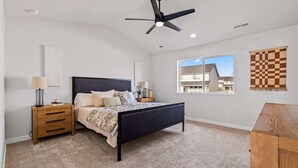 A bedroom with a bed, nightstands, a ceiling fan, a window, and a checkered wall hanging. - Luxury 5BR Retreat • Hot Tub • Game Room • EV (Meridian)