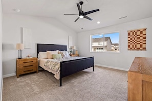 A bedroom with a bed, nightstands, a ceiling fan, a window, and a checkered wall hanging. - Luxury 5BR Retreat • Hot Tub • Game Room • EV (Meridian)
