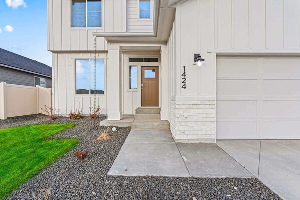 A two-story house with a front entrance, a garage, and a well-maintained lawn. - Luxury 5BR Retreat • Hot Tub • Game Room • EV (Meridian)