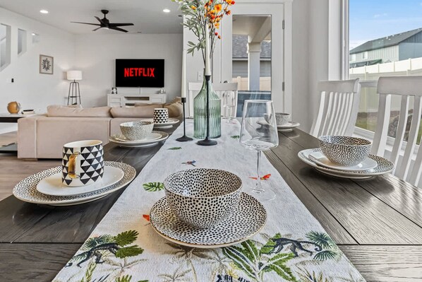 Un comedor moderno con una mesa larga dispuesta para cuatro personas, con vajilla estampada y un centro de mesa decorativo.