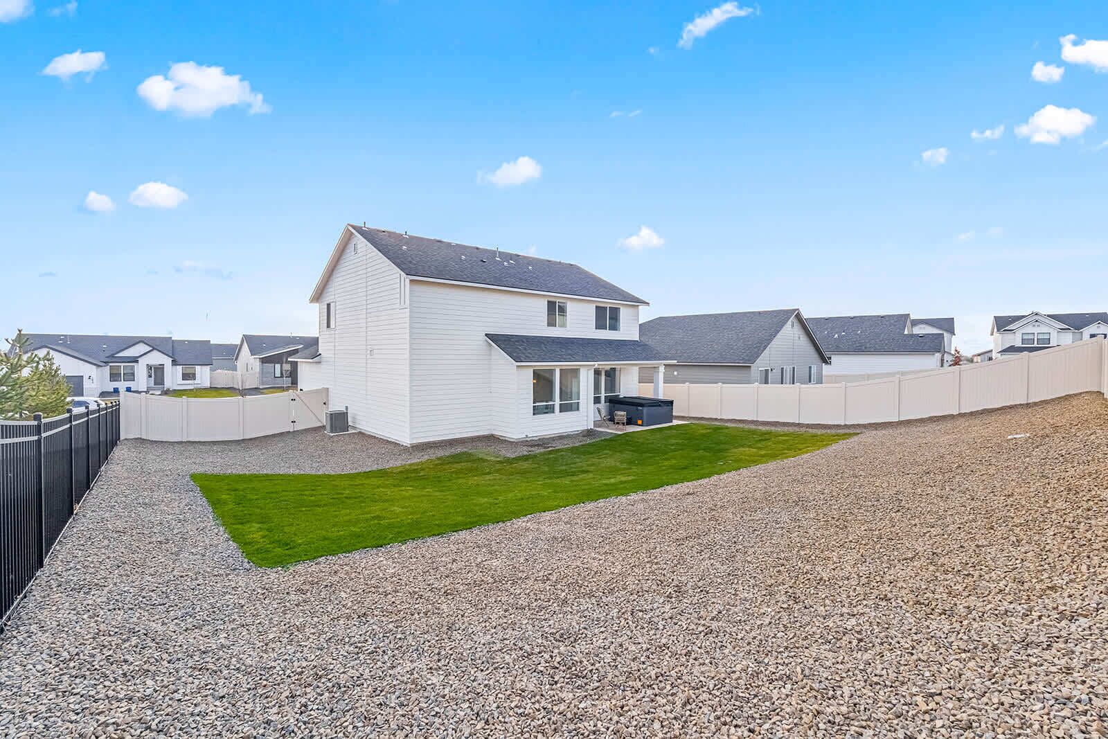 A residential area with a white house, a well-maintained lawn, and a gravel driveway.