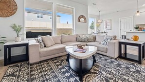 A modern living room with a beige sectional sofa, a round coffee table, and patterned rugs. - Luxury 5BR Retreat • Hot Tub • Game Room • EV (Meridian)