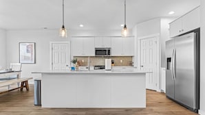 A modern kitchen with a central island, stainless steel appliances, and pendant lighting. - Luxury 5BR Retreat • Hot Tub • Game Room • EV (Meridian)