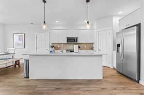 A modern kitchen with a central island, stainless steel appliances, and pendant lighting. - Luxury 5BR Retreat • Hot Tub • Game Room • EV (Meridian)
