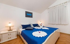 A neatly made bed with blue bedding, white pillows, and a decorative towel arrangement. There is a bedside table with a lamp, a framed picture on the wall, and a window with white curtains. - Pet friendly apartment in Bol with lake view (Bol)